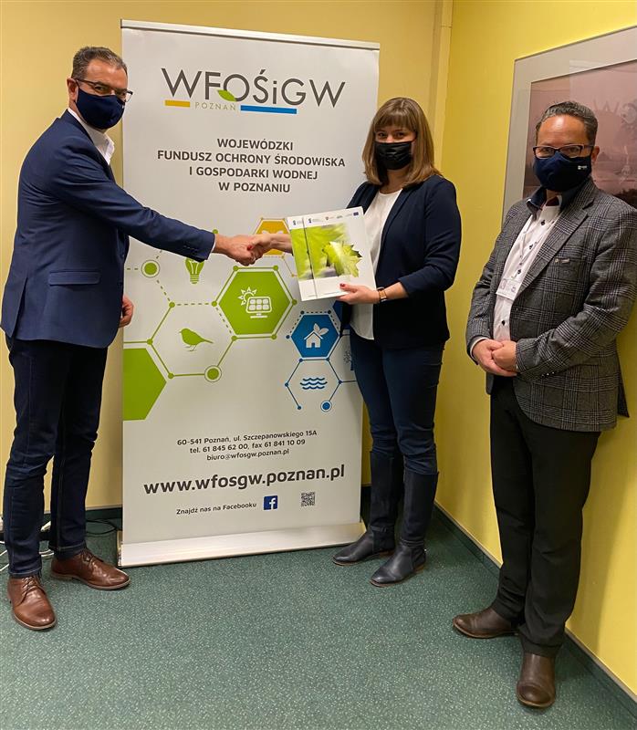 Podpisanie umowy: na tle rollapu WFOŚiGW w Poznaniu stoją Aleksandra Durkowska, Zastępca Prezesa WFOŚiGW w Poznaniu, Sławomir Lorek, Prezes Zarządu MPEC-Konin Sp. z o.o. oraz Jacek Slanin, Dyrektor Projektów i Marketingu. Wszyscy mają maseczki na twarzach. Pani Prezes z Prezesem MPEC-Konin wspólnie trzymają teczkę z umową.