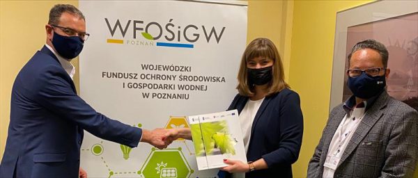 Podpisanie umowy: na tle rollapu WFOŚiGW w Poznaniu stoją Aleksandra Durkowska, Zastępca Prezesa WFOŚiGW w Poznaniu, Sławomir Lorek, Prezes Zarządu MPEC-Konin Sp. z o.o. oraz Jacek Slanin, Dyrektor Projektów i Marketingu. Wszyscy mają maseczki na twarzach. Pani Prezes z Prezesem MPEC-Konin wspólnie trzymają teczkę z umową.