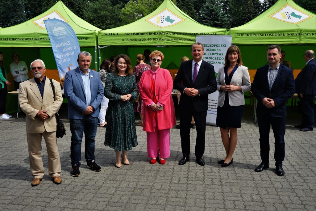 7 osób stoi na tle stoisk wystawienniczych na świeżym powietrzu.
