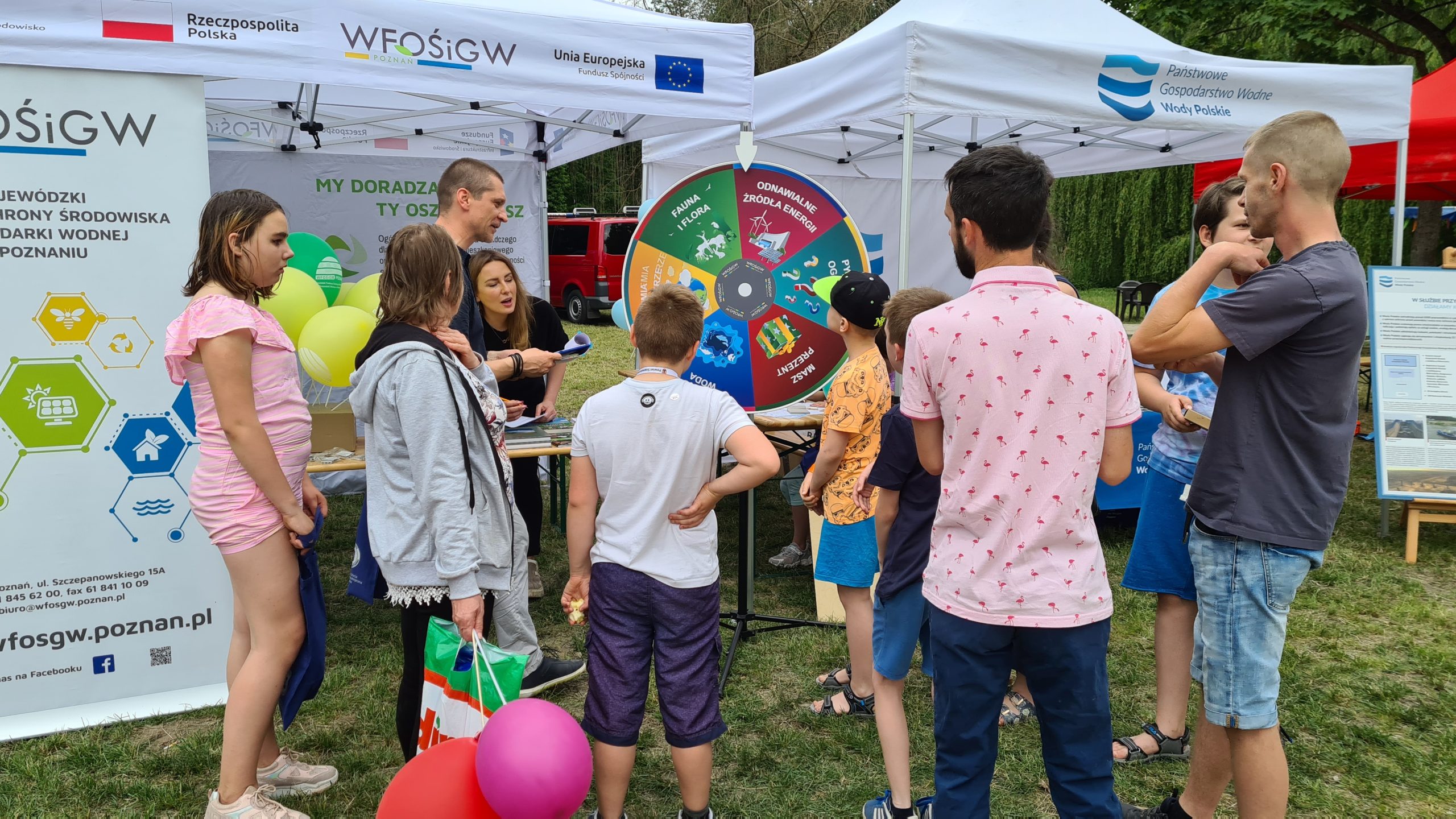 Grupa ludzi na tle stoiska w trakcie pikniku.