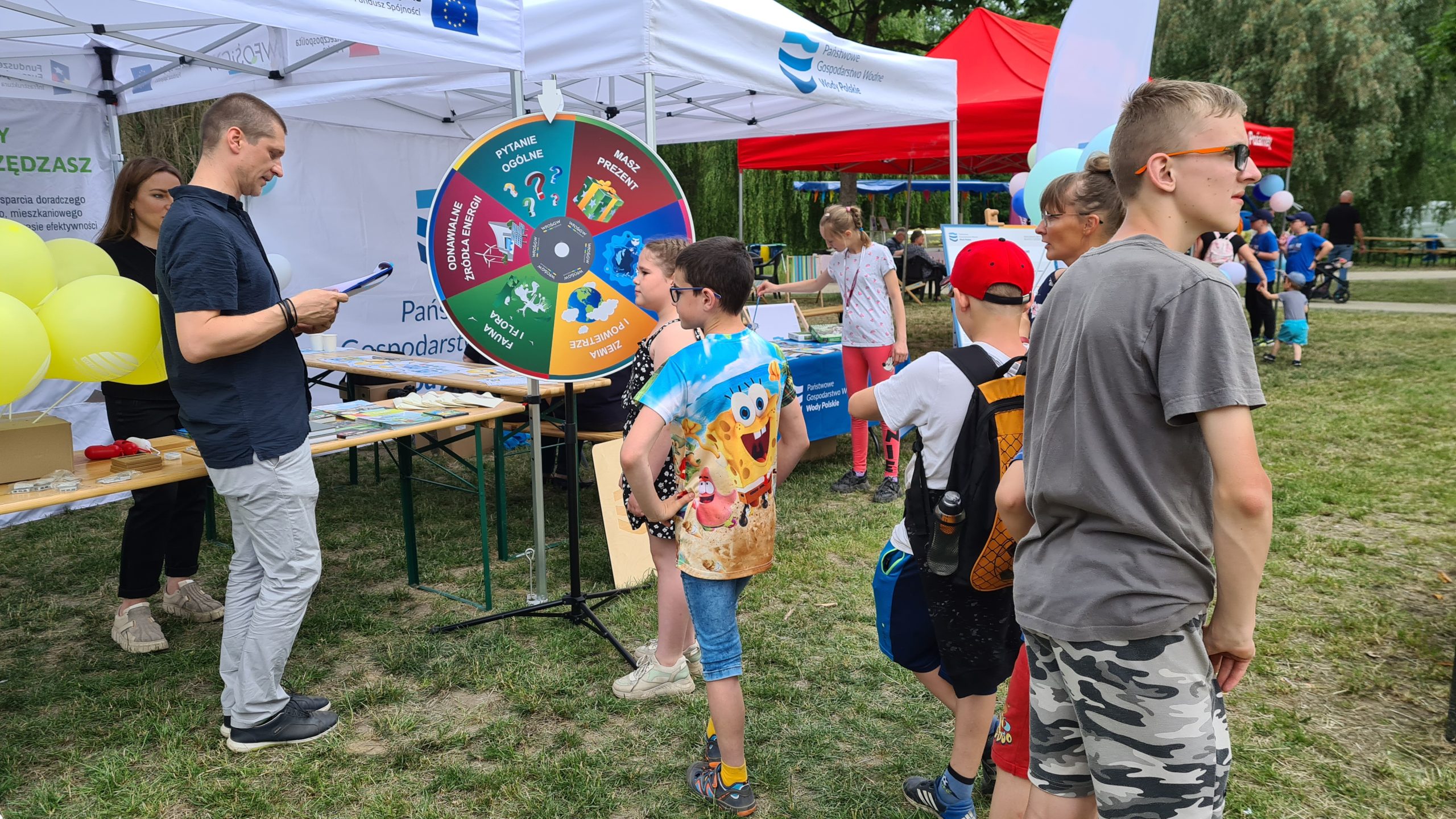 Grupa ludzi na tle stoiska w trakcie pikniku.