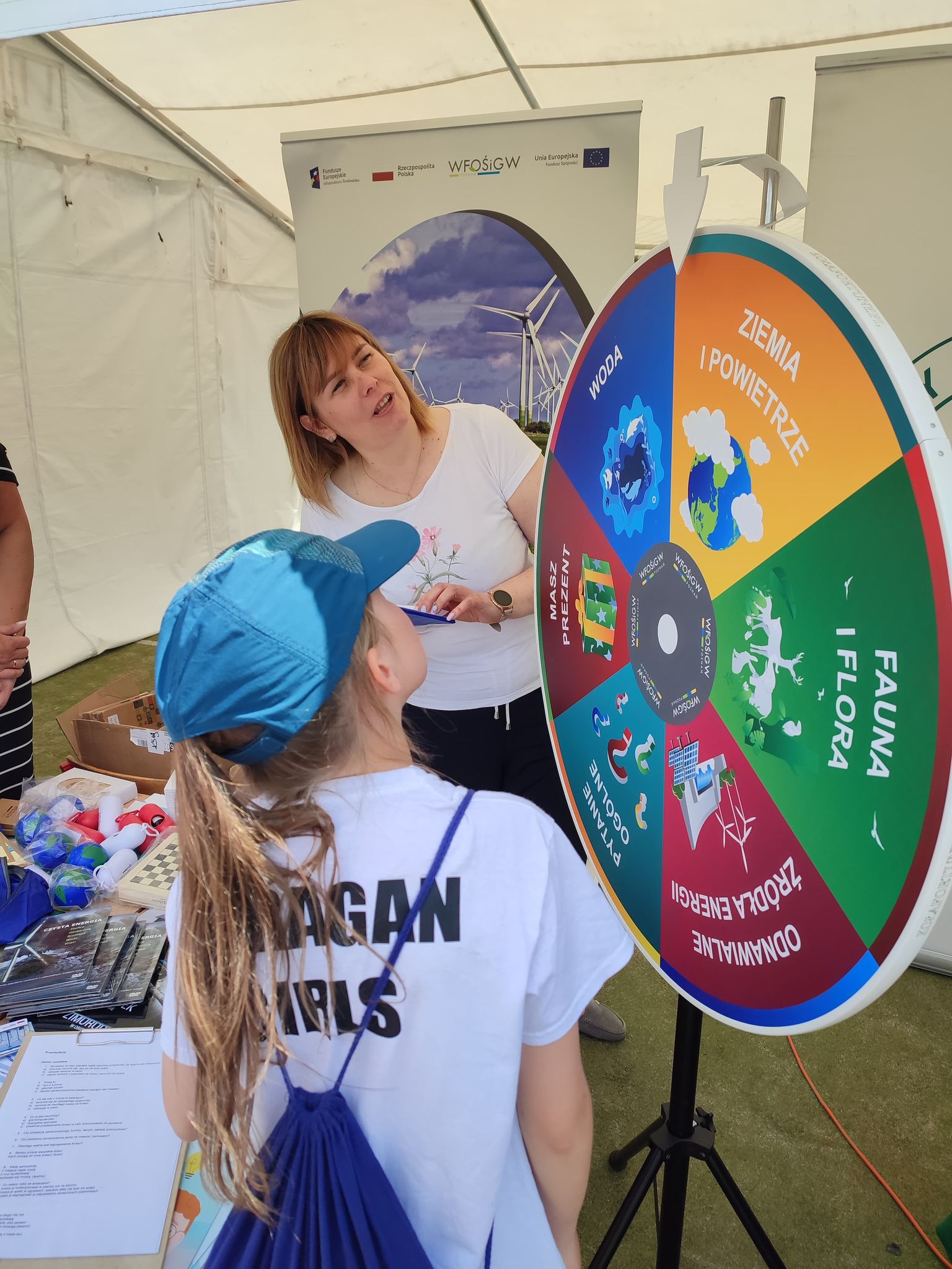 2 osoby wokół stoiska wystawienniczego podczas festynu.