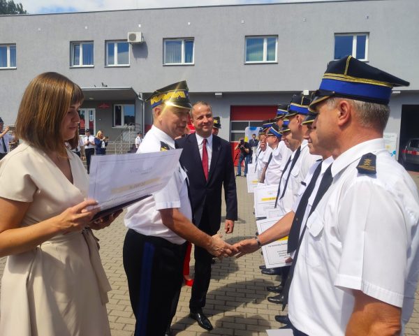 Szereg strażaków stoi na świżym powietrzu.