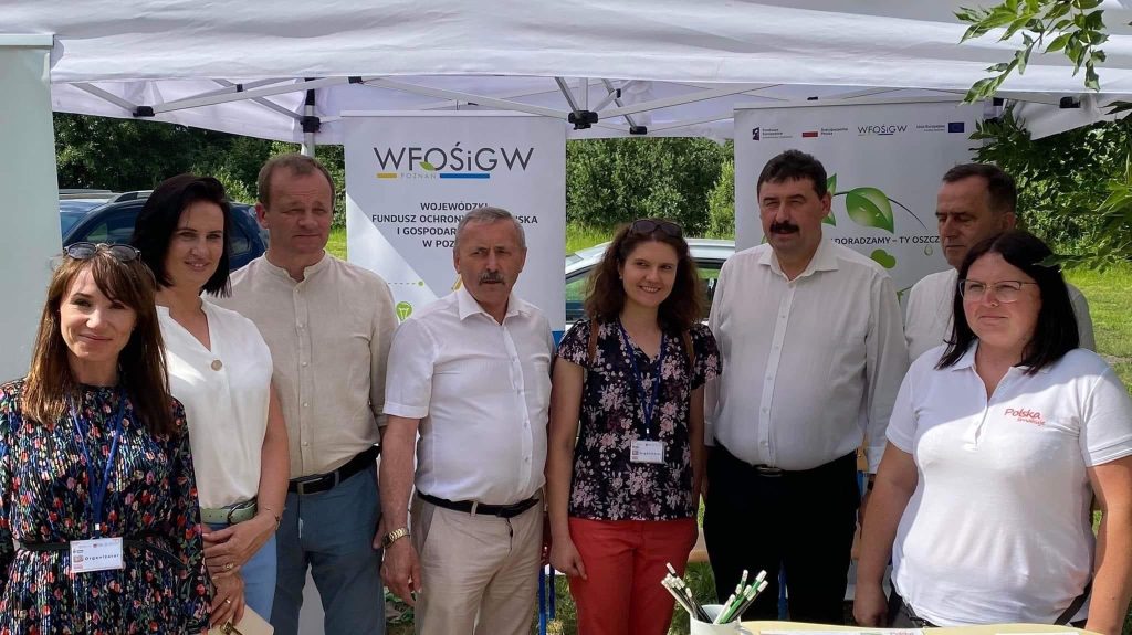 Grupa osób stoi przy stoisku podczas festynu.