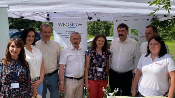 Grupa osób stoi przy stoisku podczas festynu.