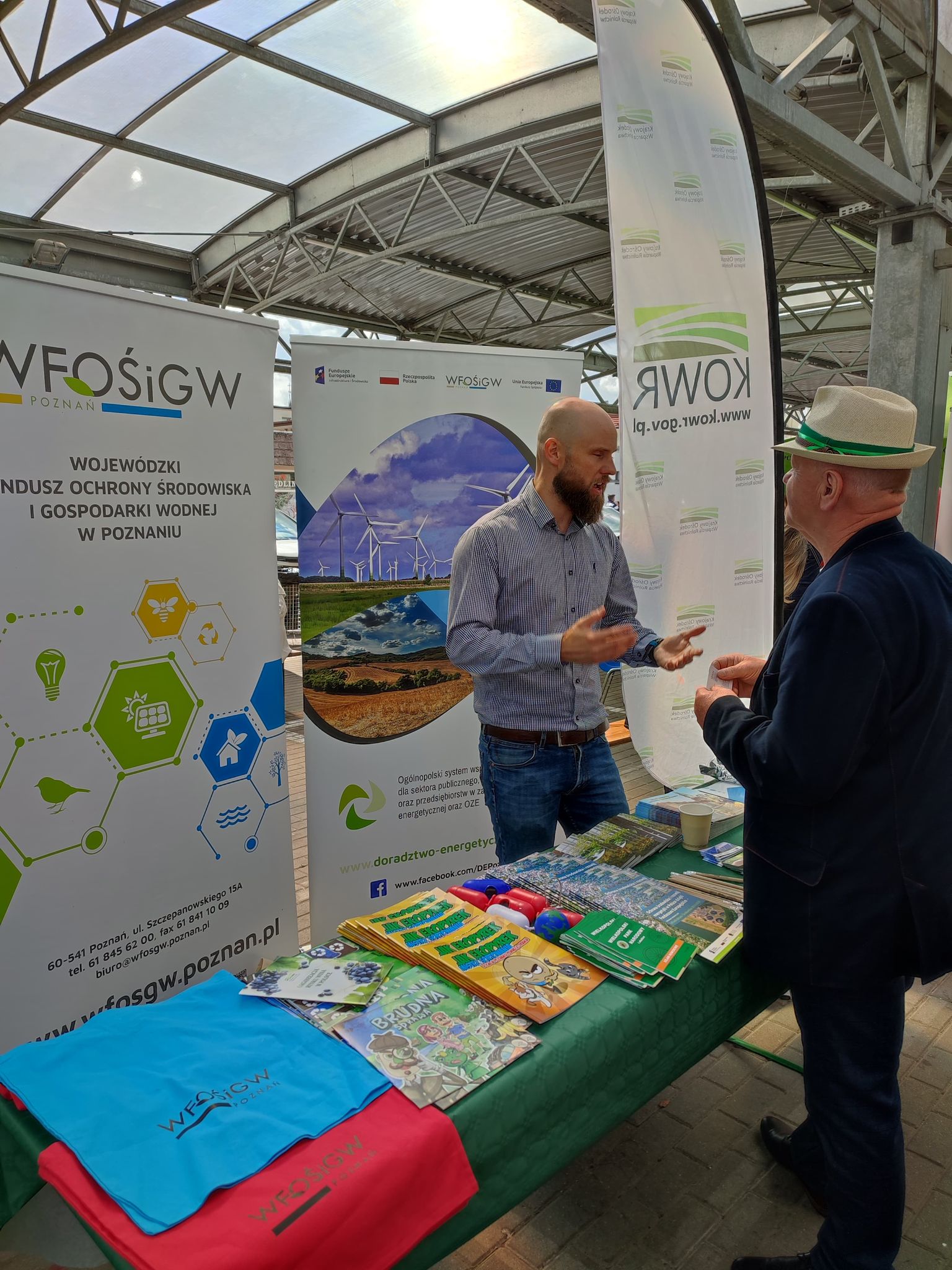 2 osoby stoją przy stoisku w trakcie festynu.