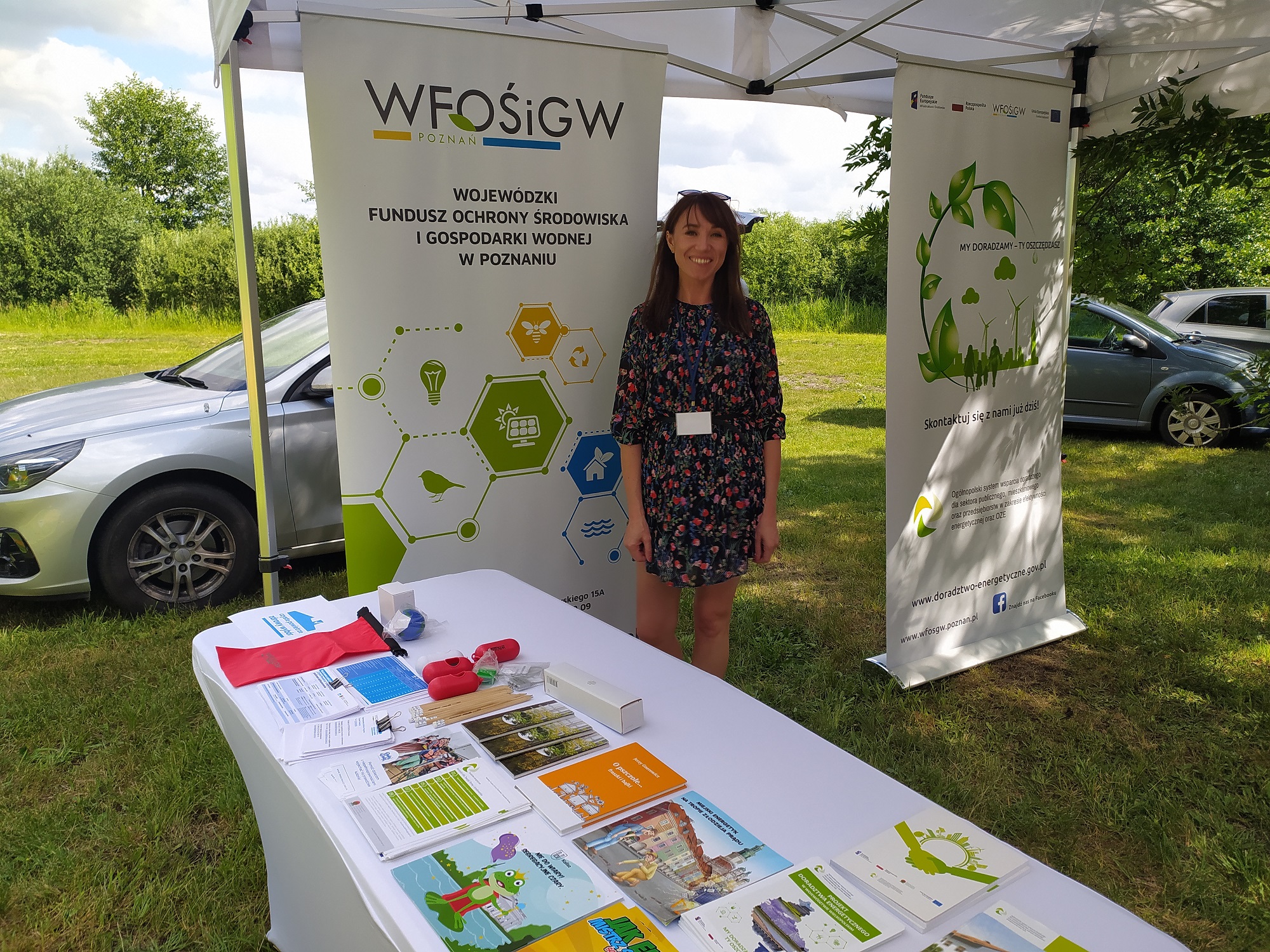 1 osoba stoi przy stoisku wystawienniczym podczas festynu.