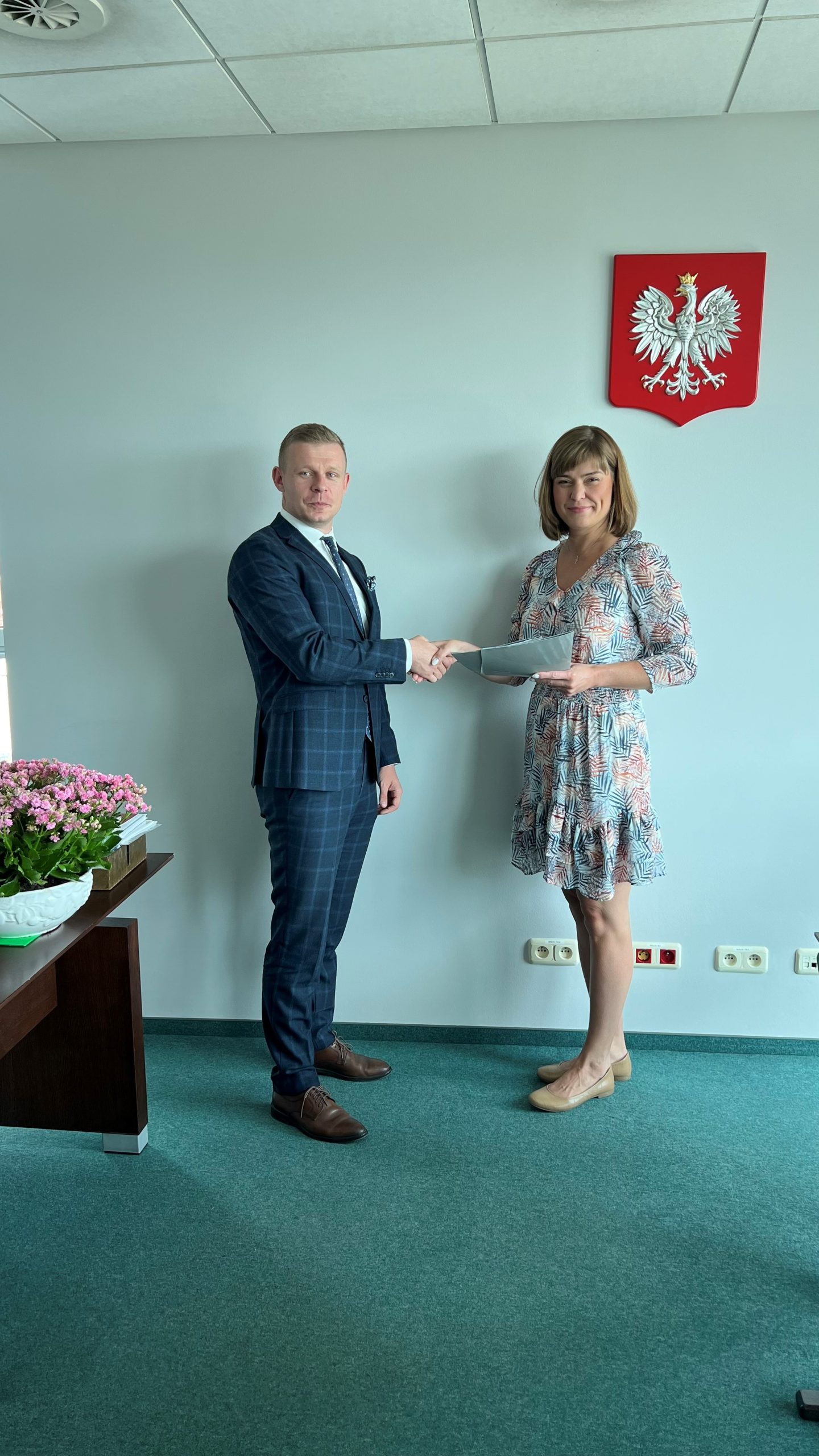 2 osoby stoją przy ścianie i podają sobie dłonie.