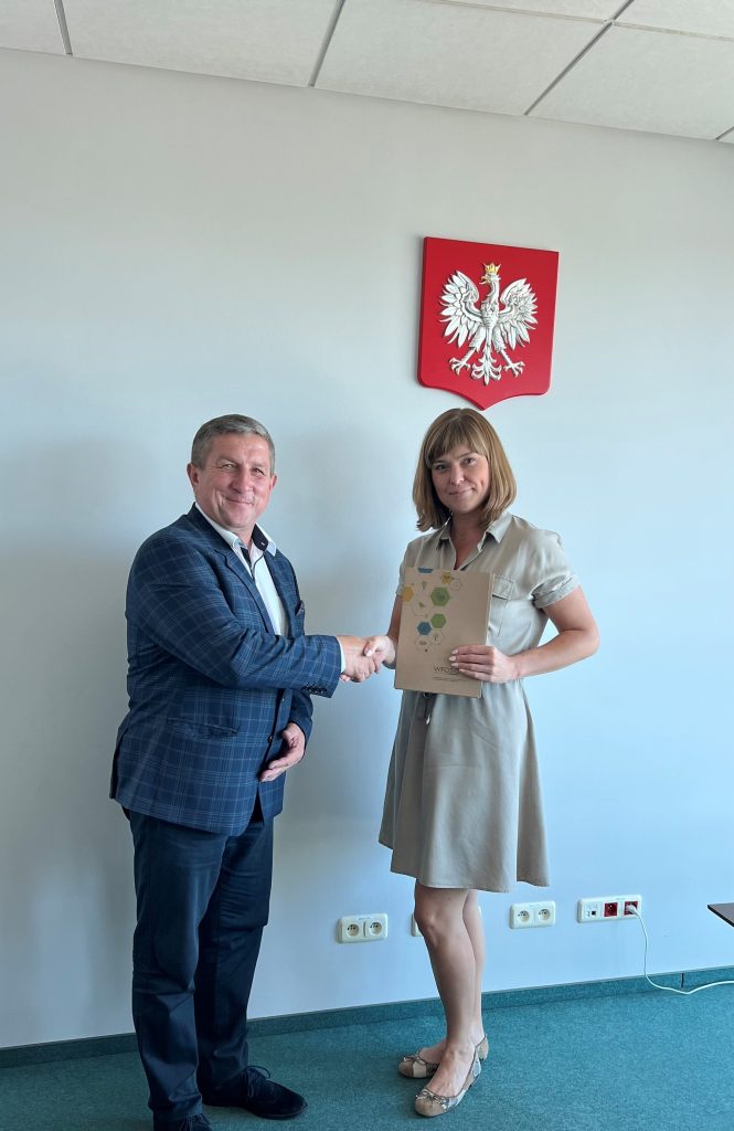 2 osoby stoją przy ścianie i podają sobie dłonie.