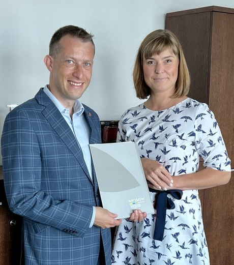 2 osoby stoją na tle ściany.