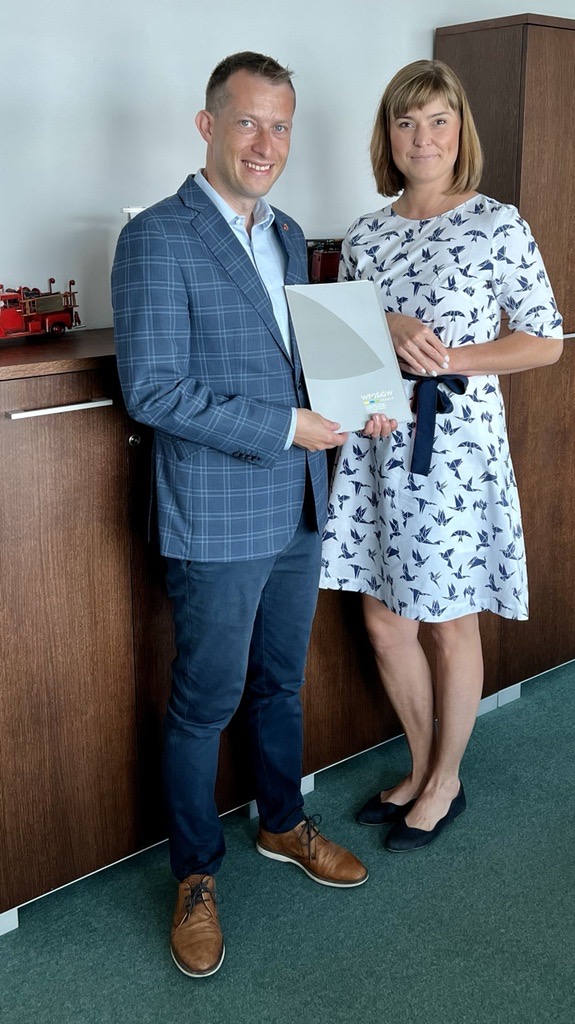 2 osoby stoją na tle ściany.