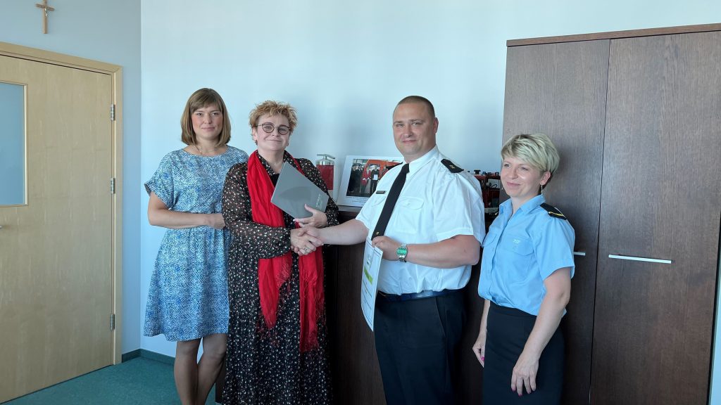 4 osoby stoją na tle ściany i mebli.