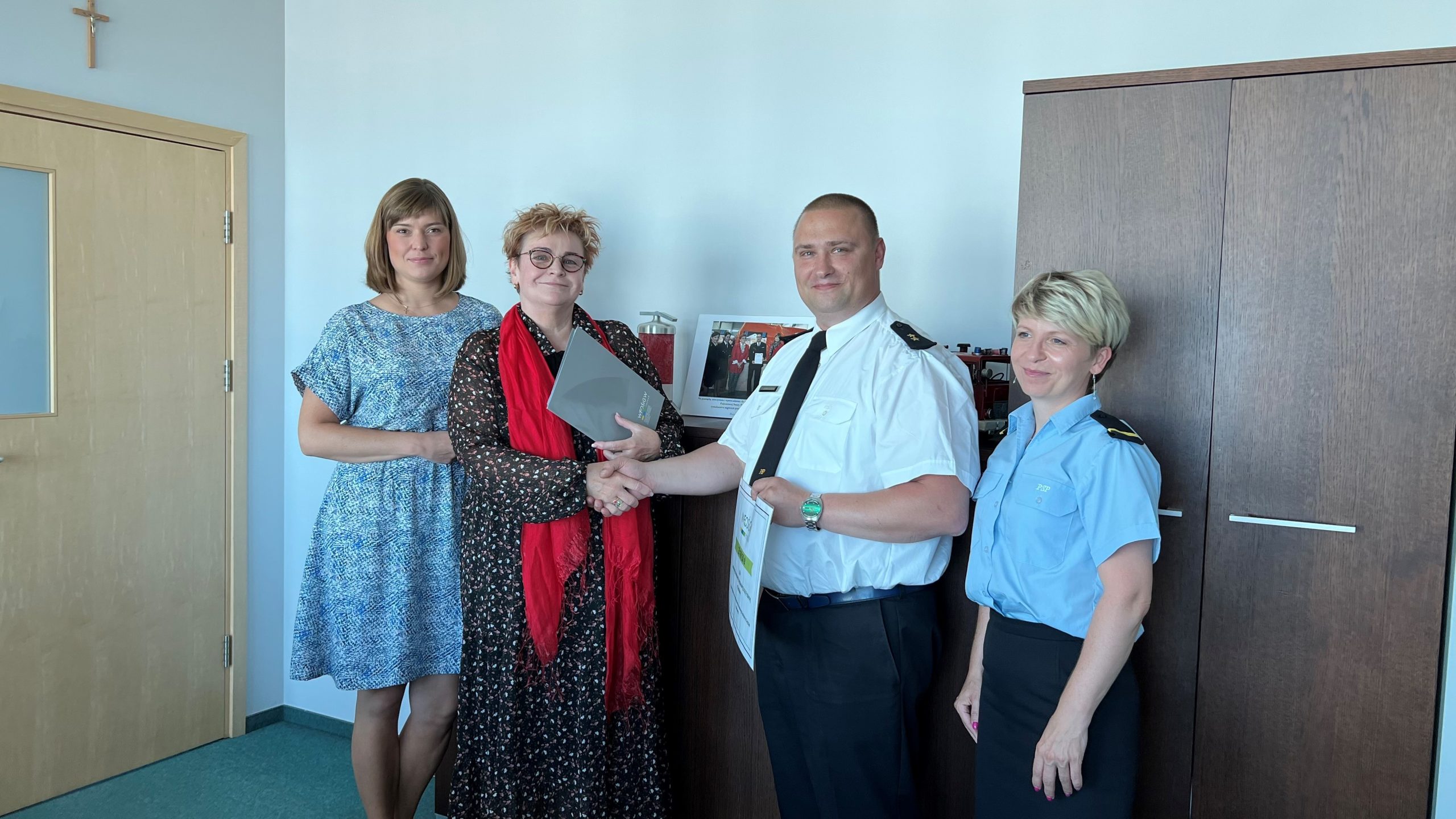 4 osoby stoją na tle ściany i mebli.