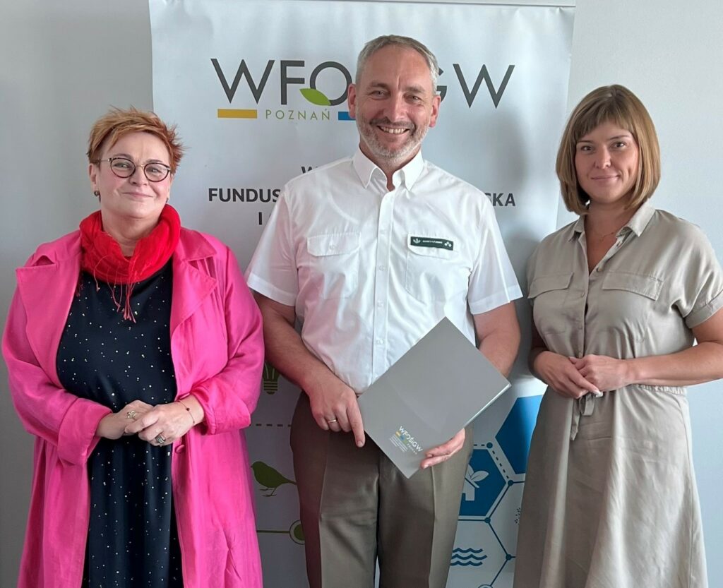 3 osoby stoją na tle ściany.