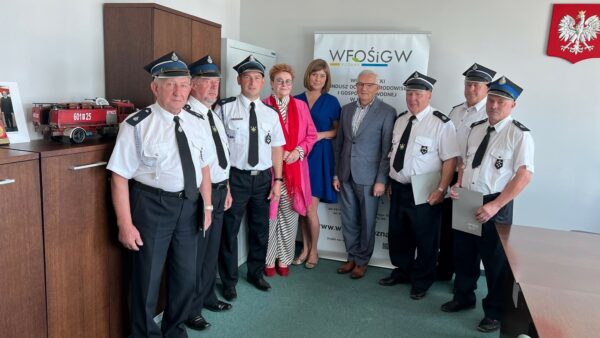 8 osób stoi na tle ściany.