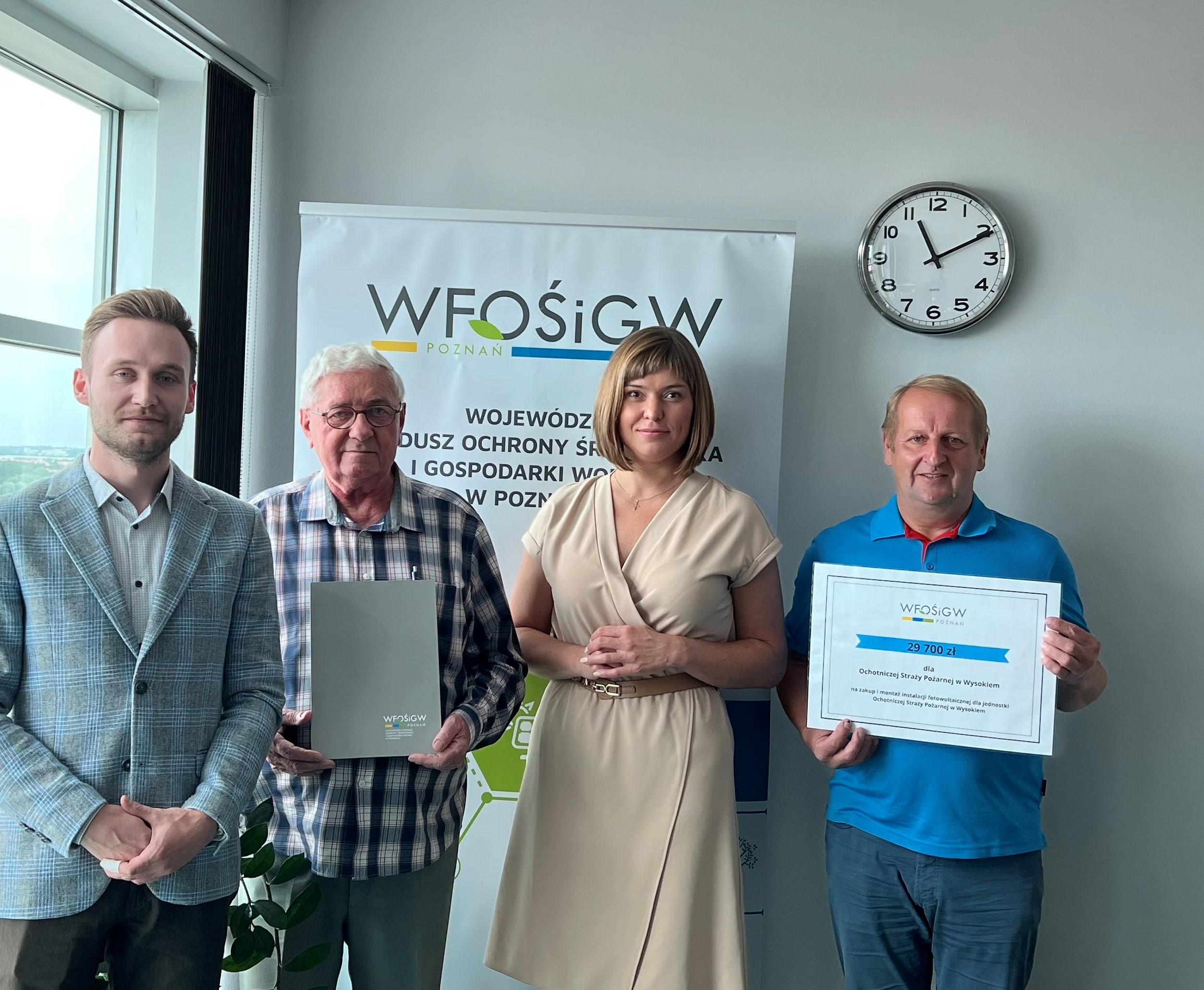 4 osoby stoją na tle ściany i okna.