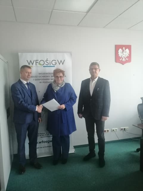 3 osoby stoją na tle ściany.