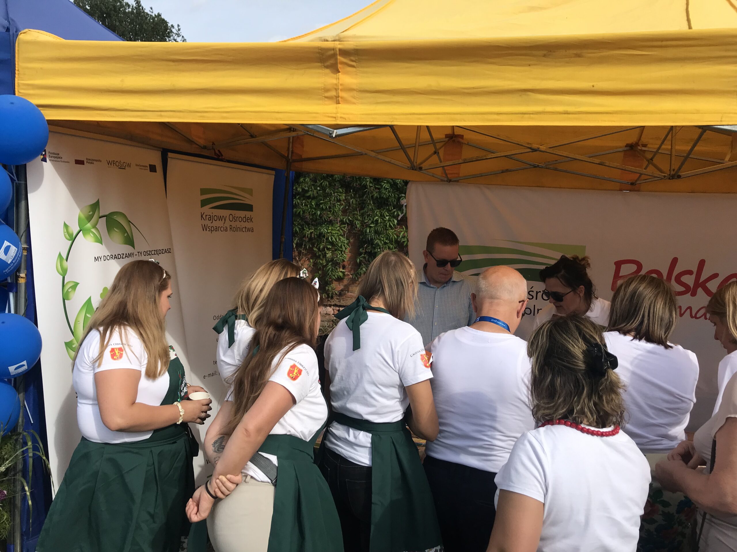 grupa osób przy stoisku wystawienniczym podczas dożynek.