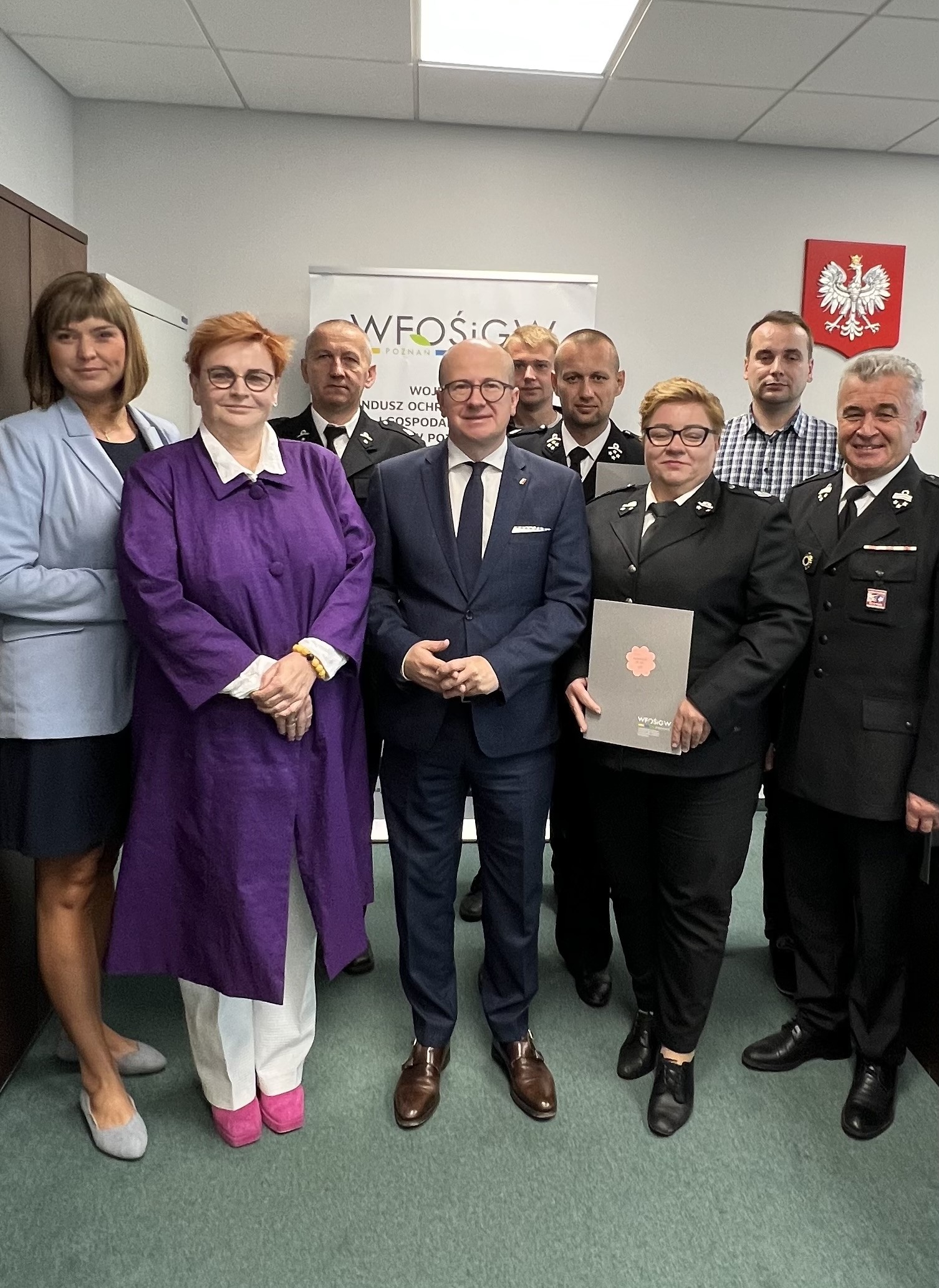 Grupa ludzi stoi na tle ściany.