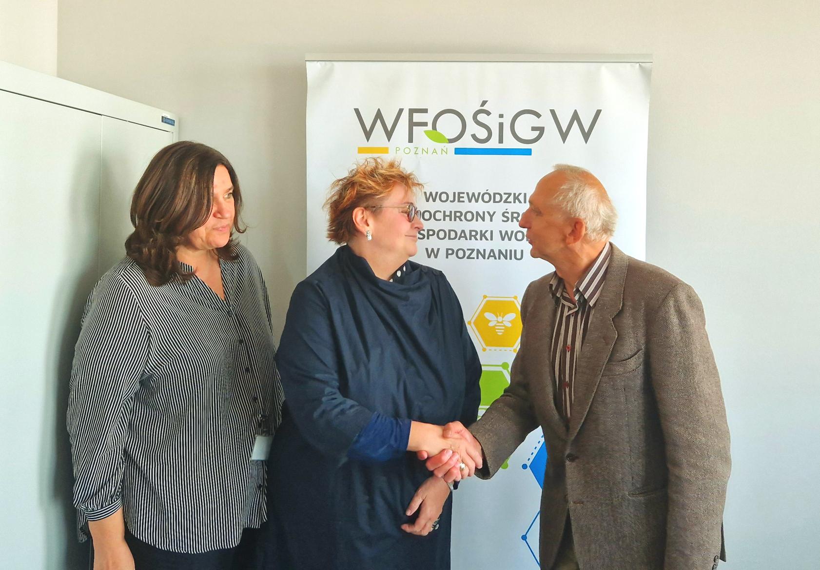 3 osoby stoją na tle ściany.