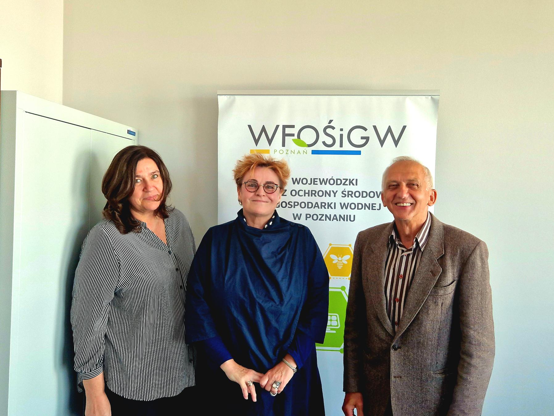 3 osoby stoją na tle ściany.