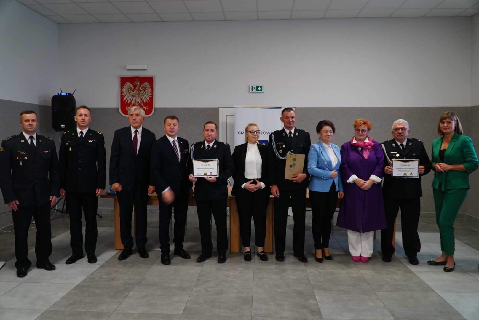 11 osób stoi na środku pomieszczenia.