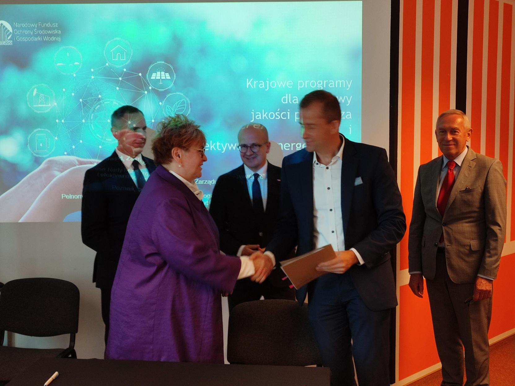 5 osób stoi, a 2 z nich podają sobie dłonie.