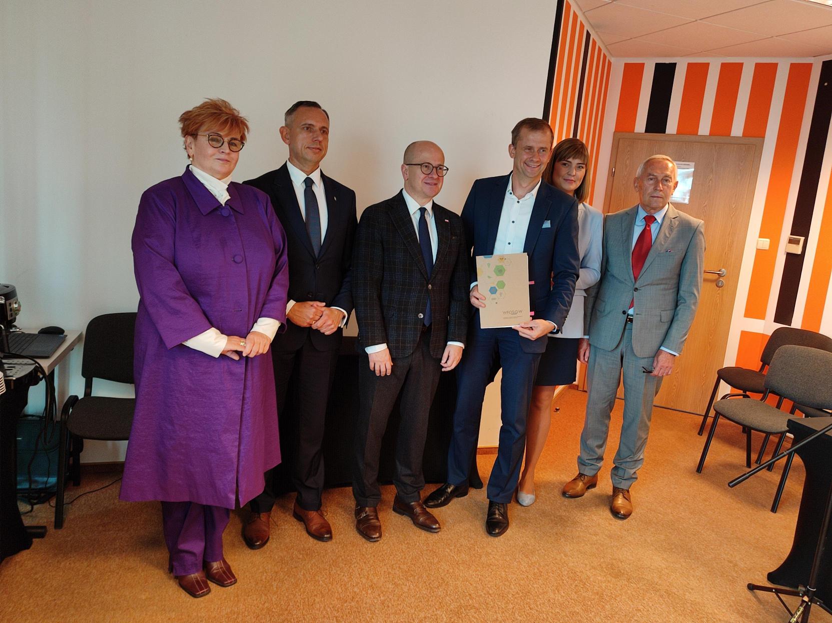 6 osób stoi przy ścianie.