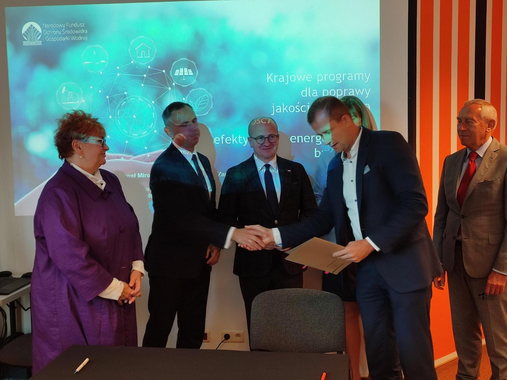 5 osób stoi, a 2 z nich podają sobie dłonie.