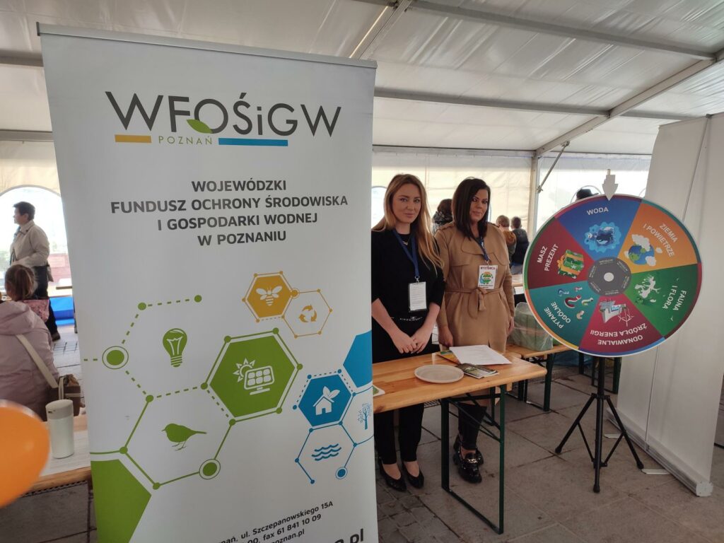 2 osoby stoją przy stoisku wystawienniczym podczas festynu.