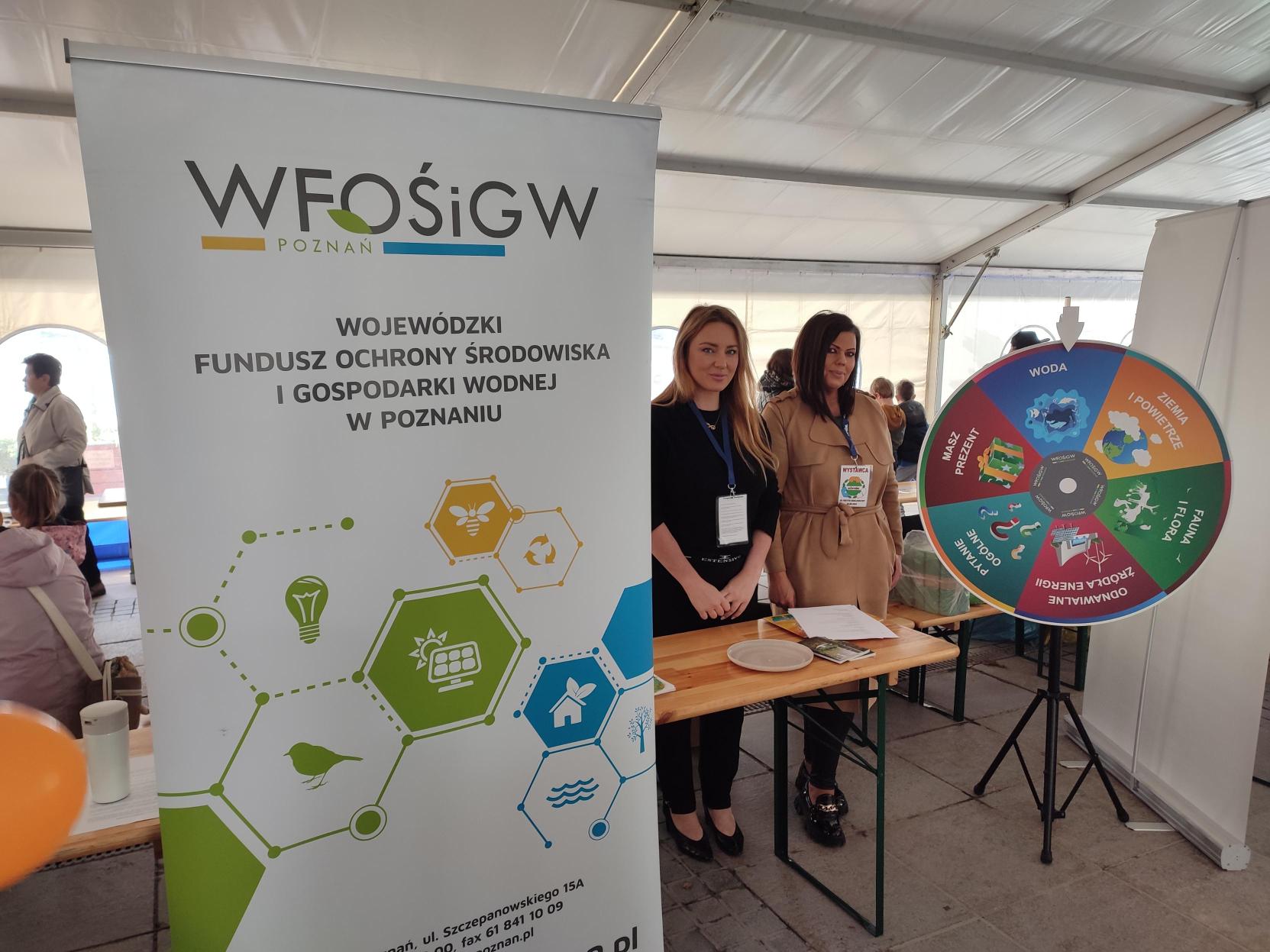 2 osoby stoją przy stoisku wystawienniczym podczas festynu.