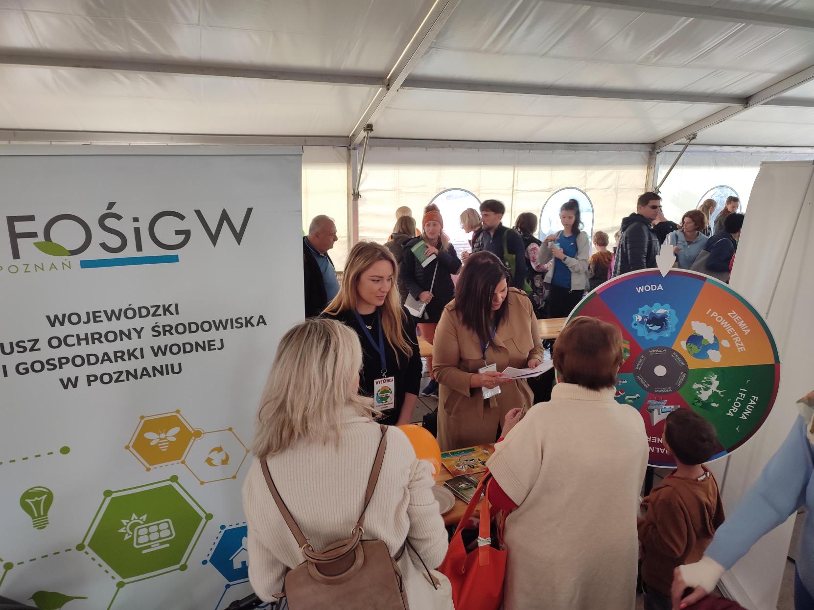 Grupka ludzi stoi przy stoisku wystawienniczym.