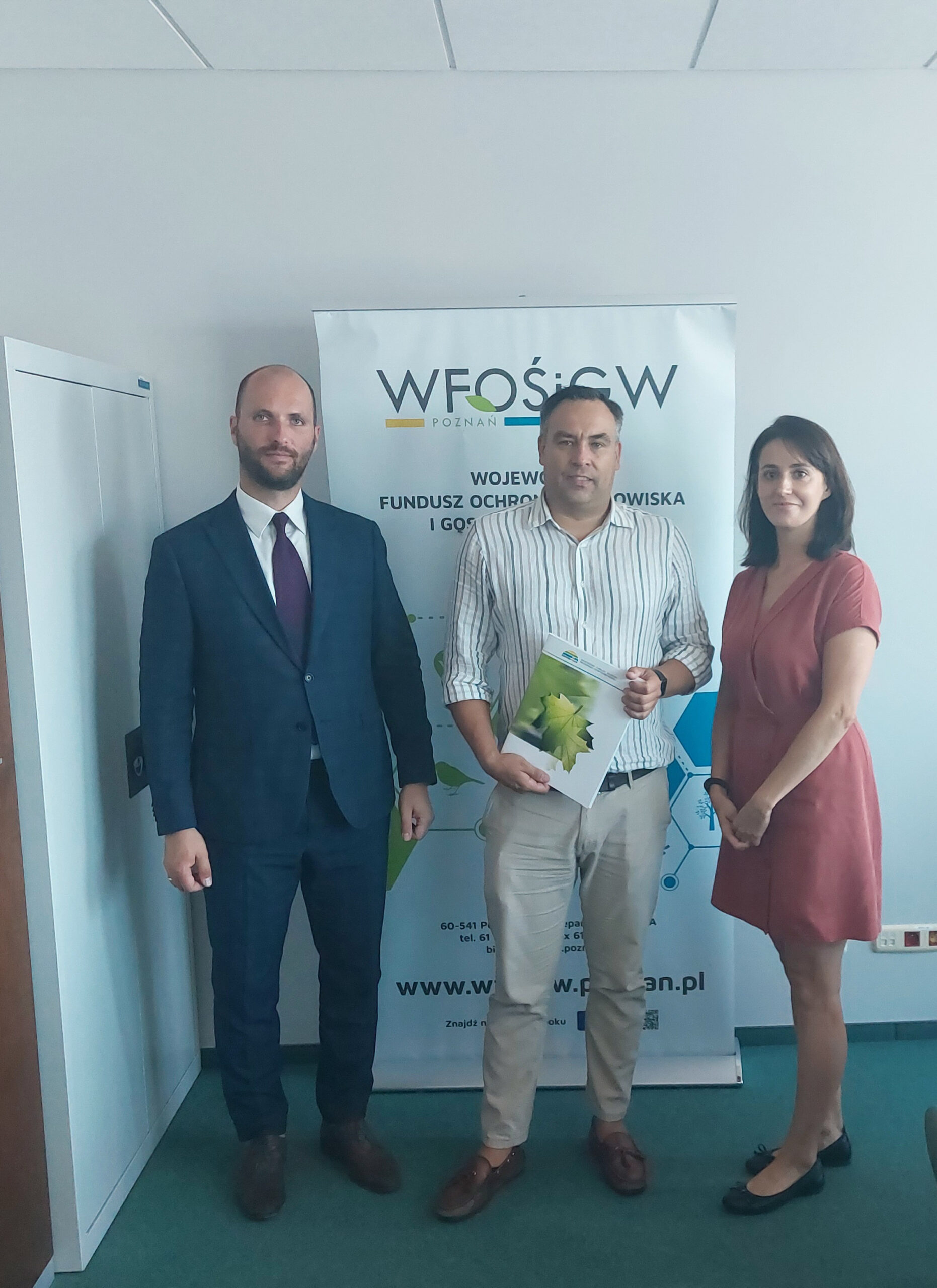 3 osoby stoją na tle ściany.