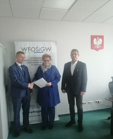 3 osoby stoją na tle ściany.