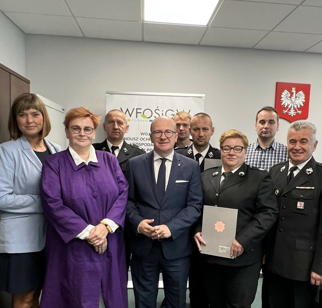 Grupa ludzi stoi na tle ściany.