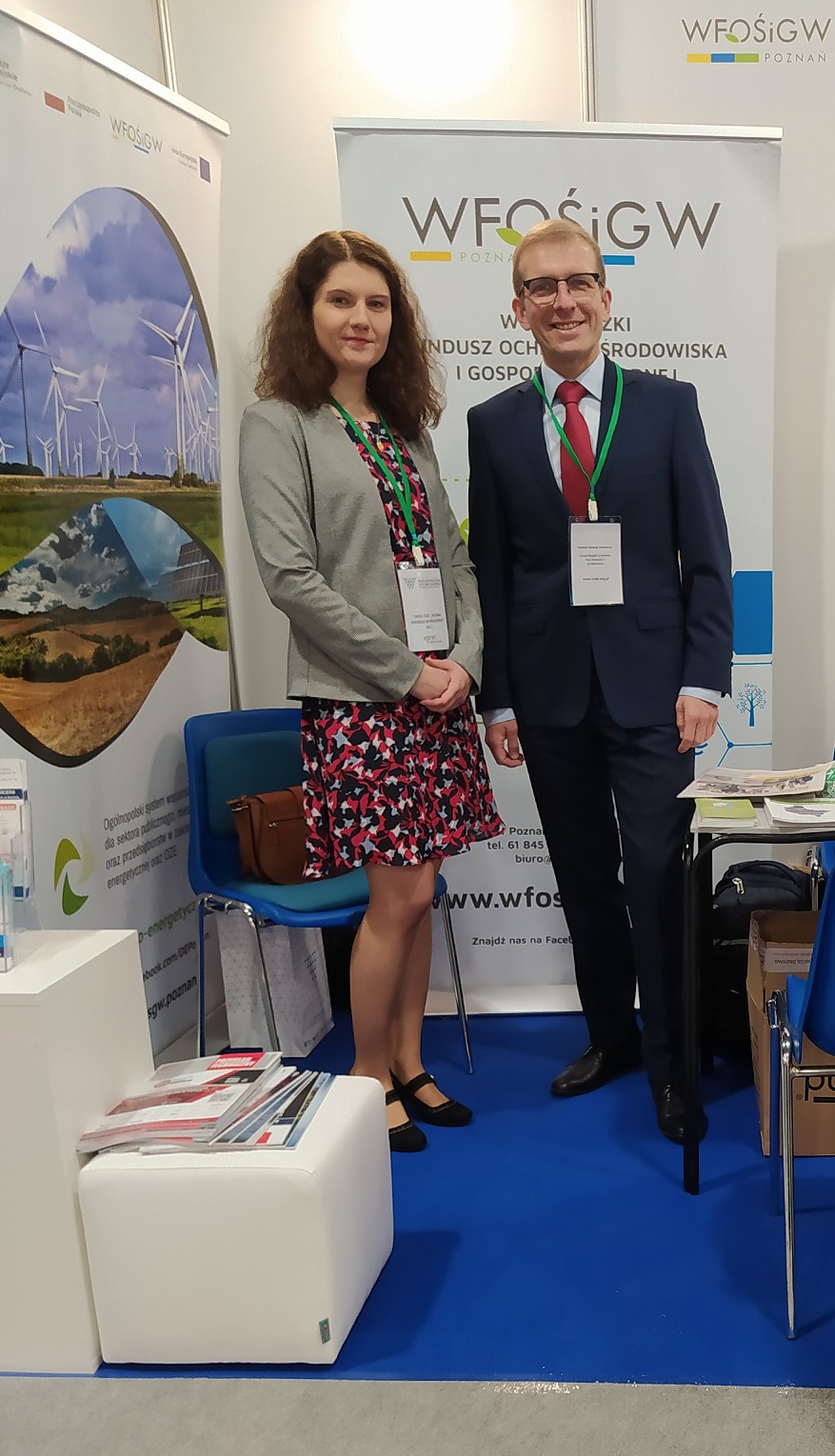 2 osoby stoją na tle ściany.