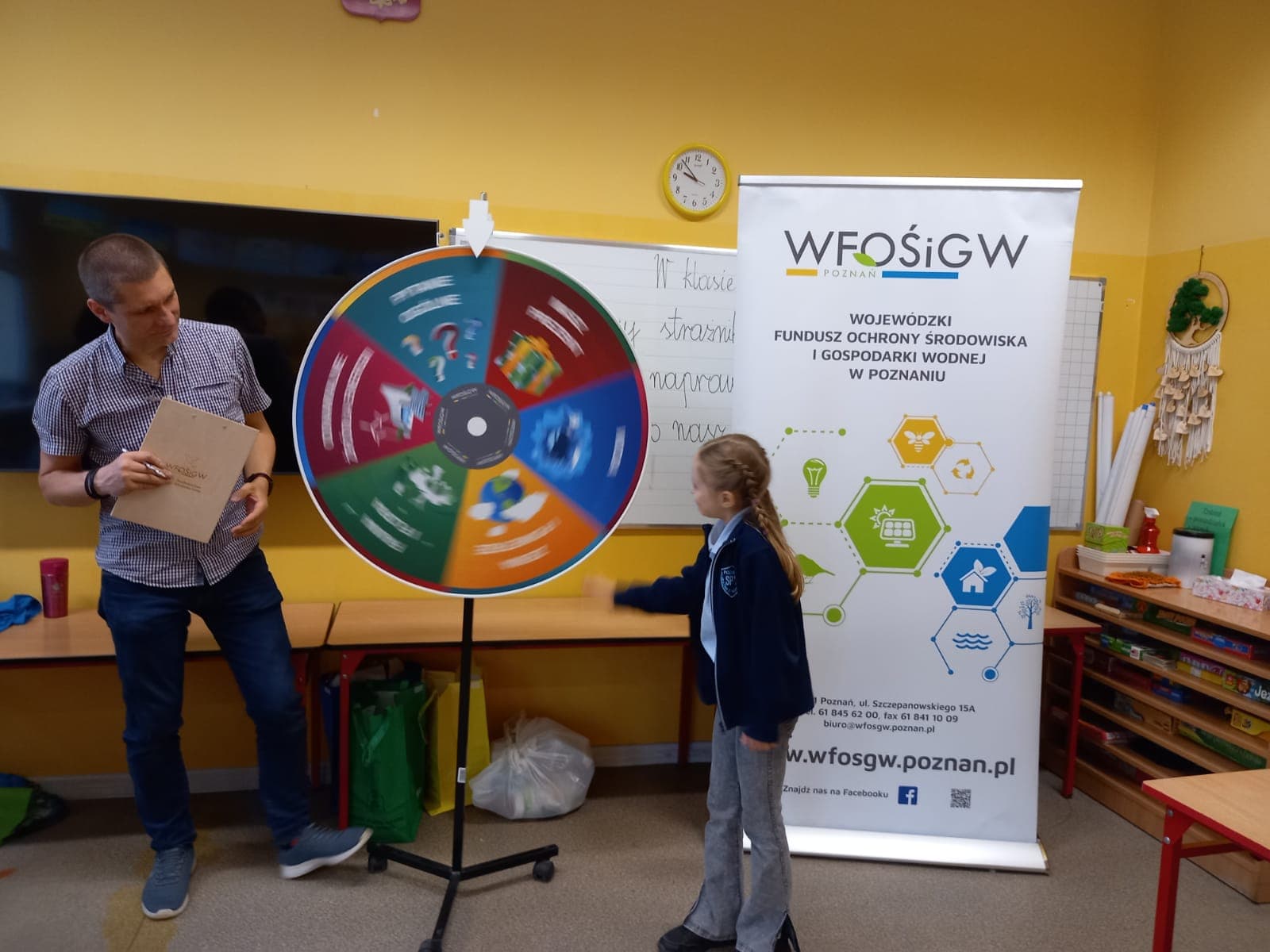 2 osoby stoją na tle ściany i tablicy lekcyjnej.