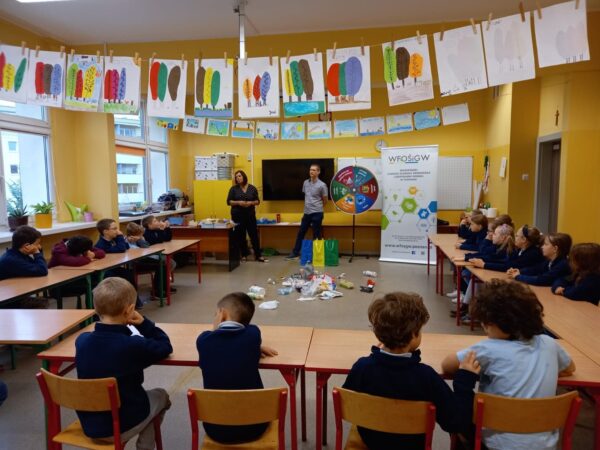 Sala lekcyjna z uczniami siedzącymi w ławkach.