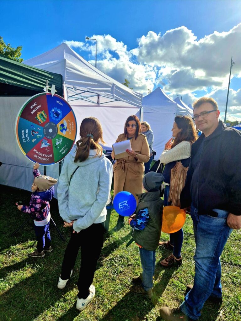 Grupa osób stoi przy stoisku na festynie.