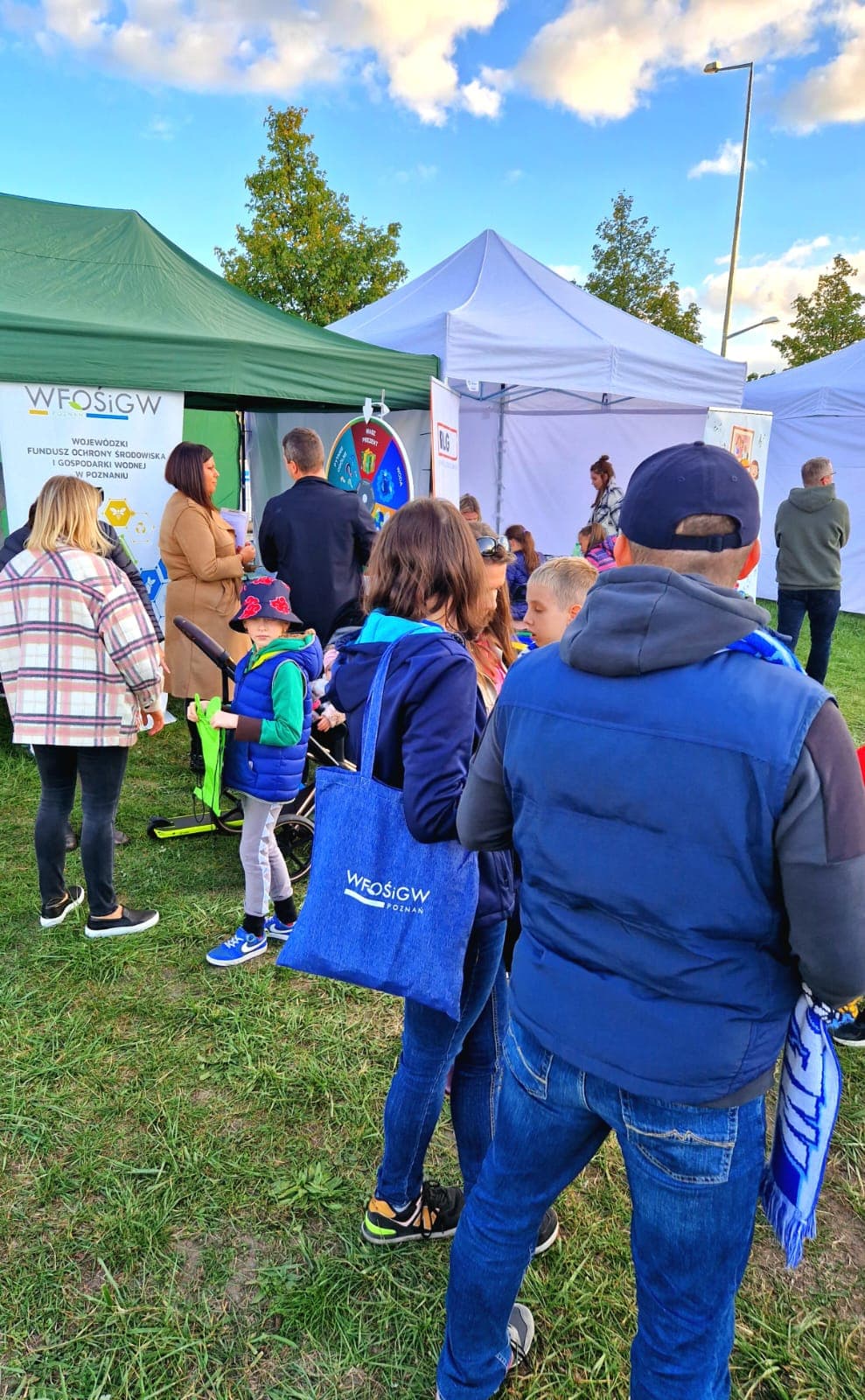 Grupa osób stoi przy stoisku na festynie.