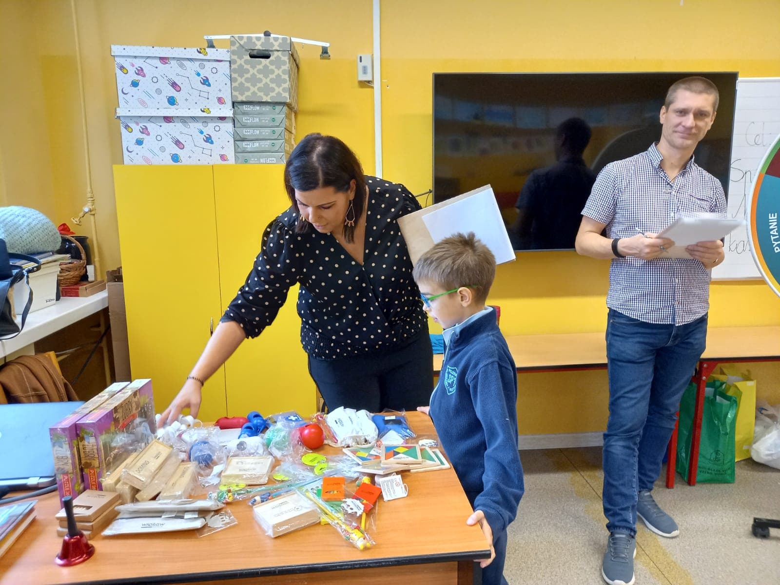 3 osoby stoja na tle ściany i obok biurka.