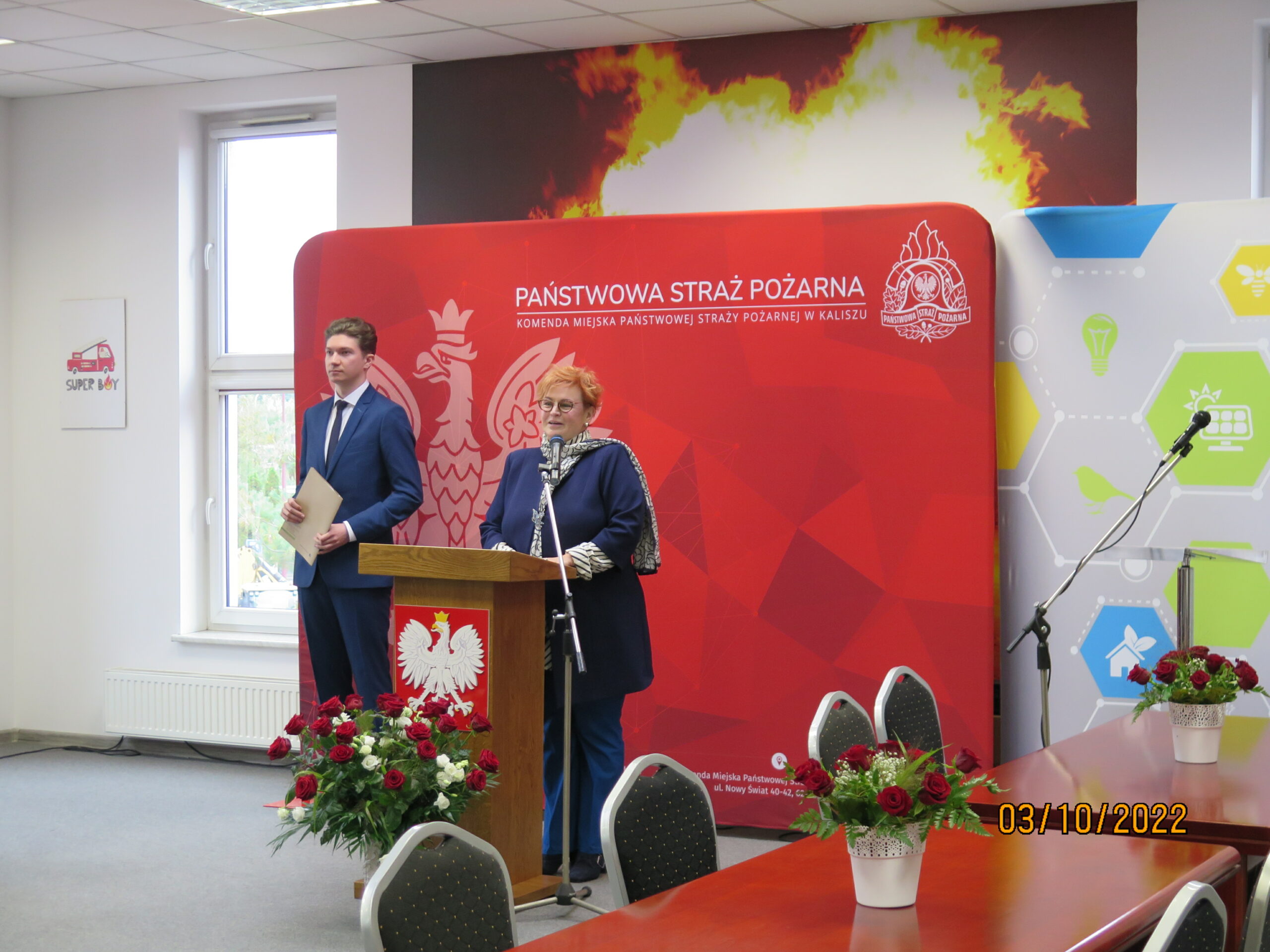 2 osoby stoją na tle ściany.