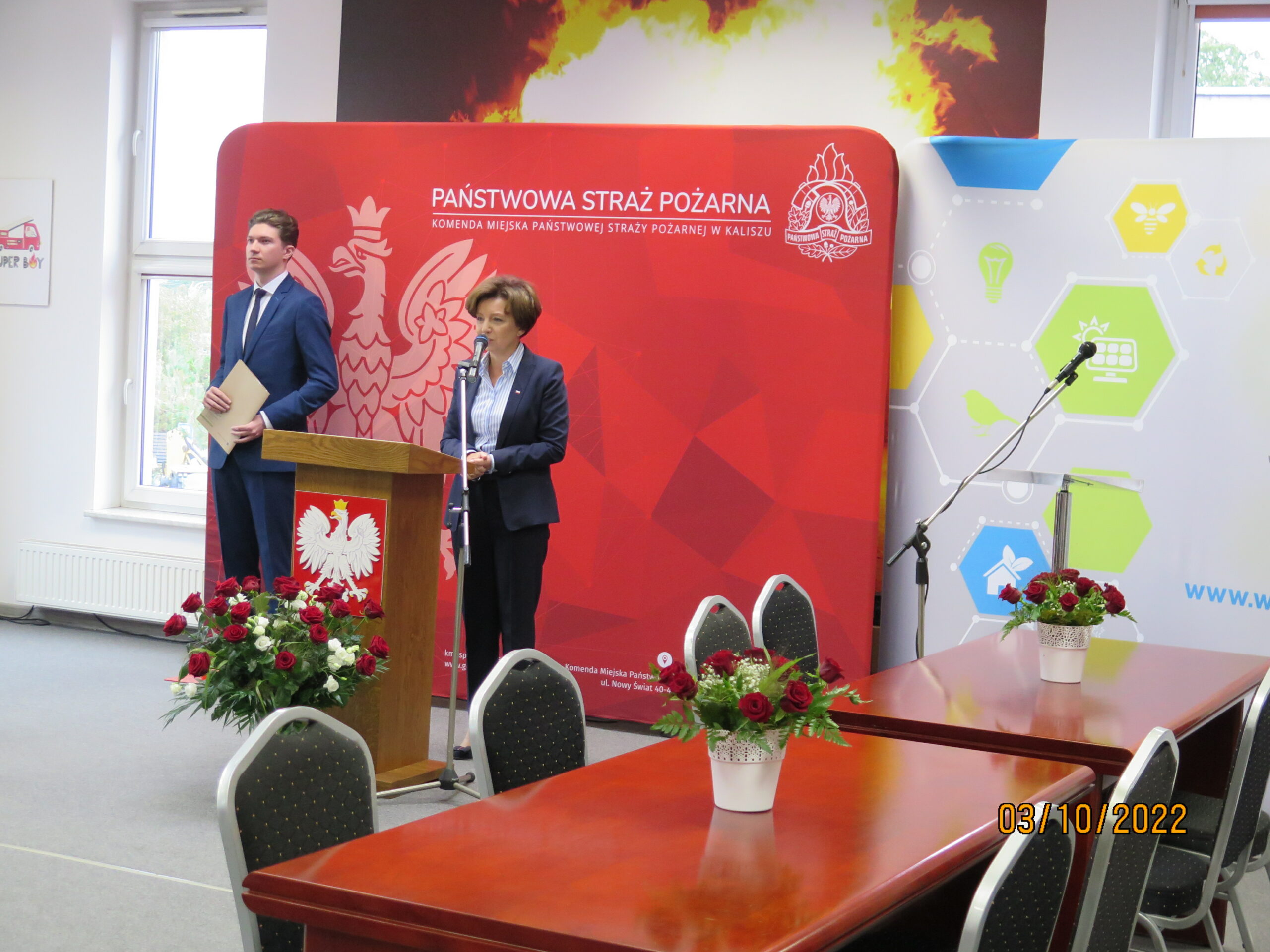 2 osoby stoją na tle ściany.