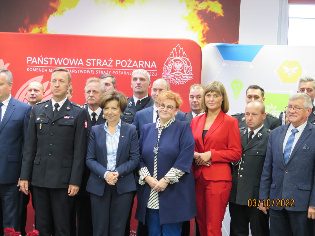 Grupa ludzi stoi na tle ściany.