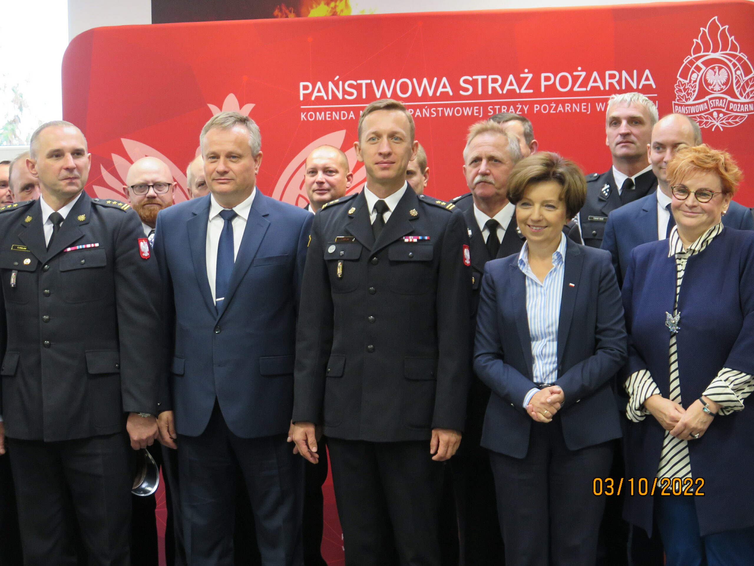 Grupa ludzi stoi na tle ściany.