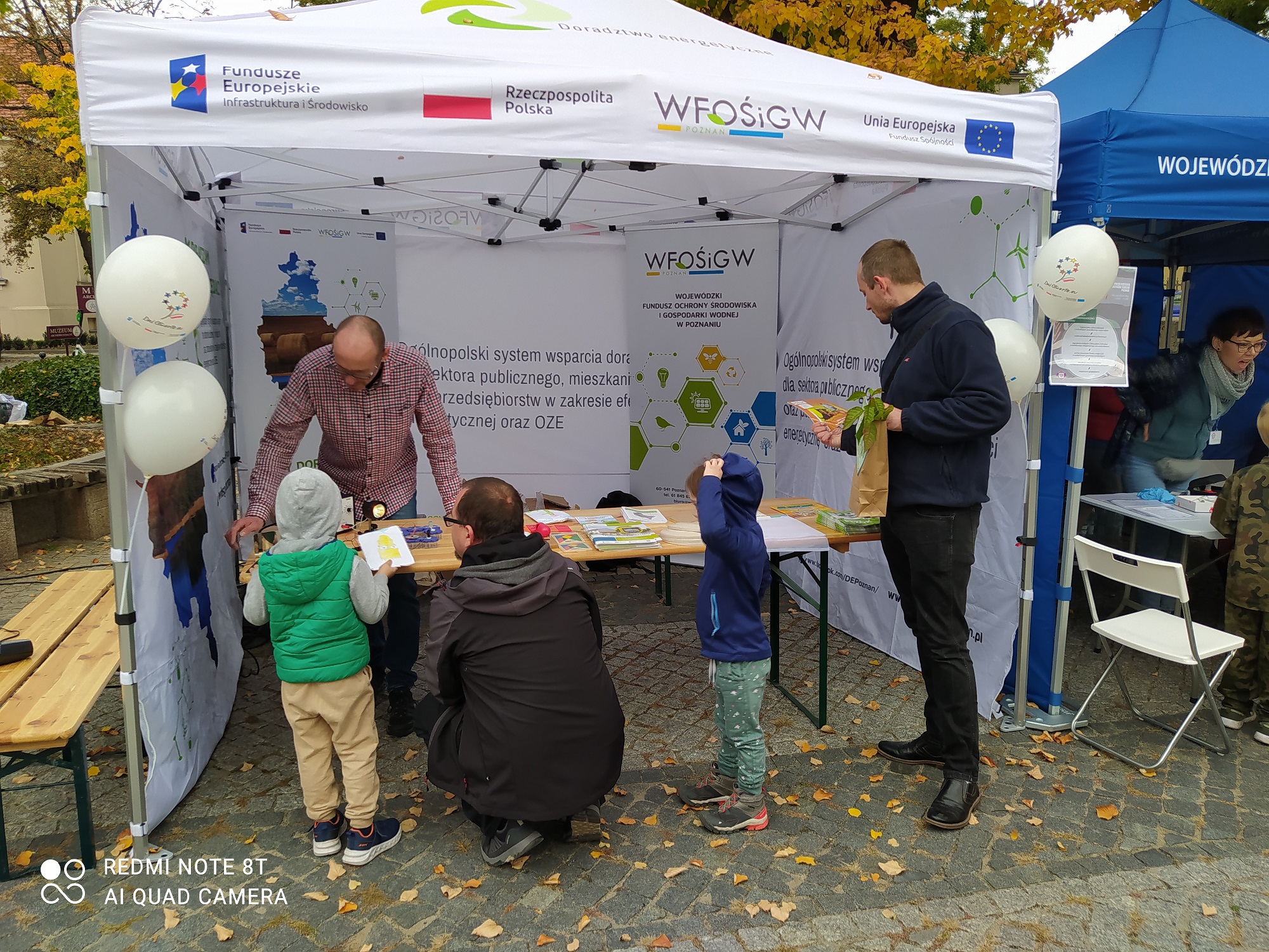 5 osób stoi przy stoisku podczas festynu.