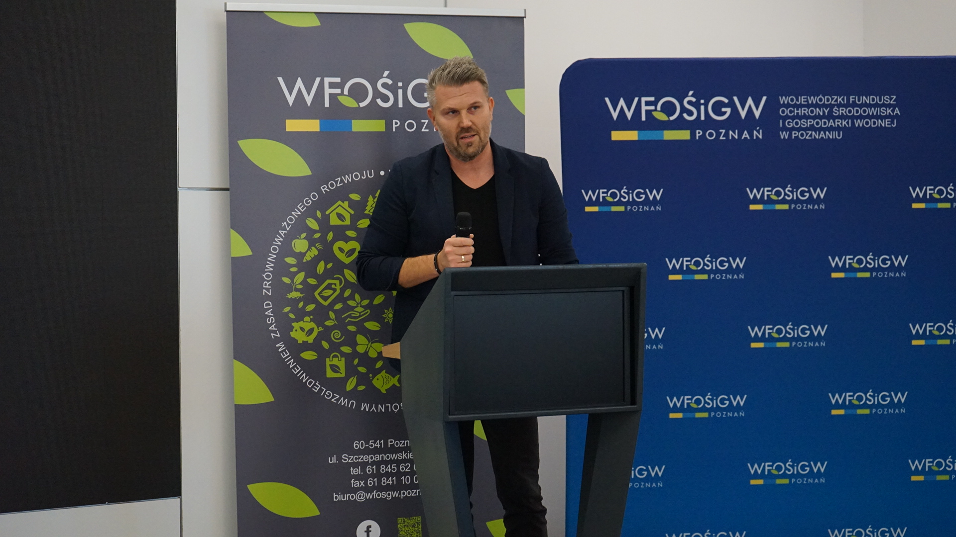 Jedna osoba stoi na scenie przy mównicy.