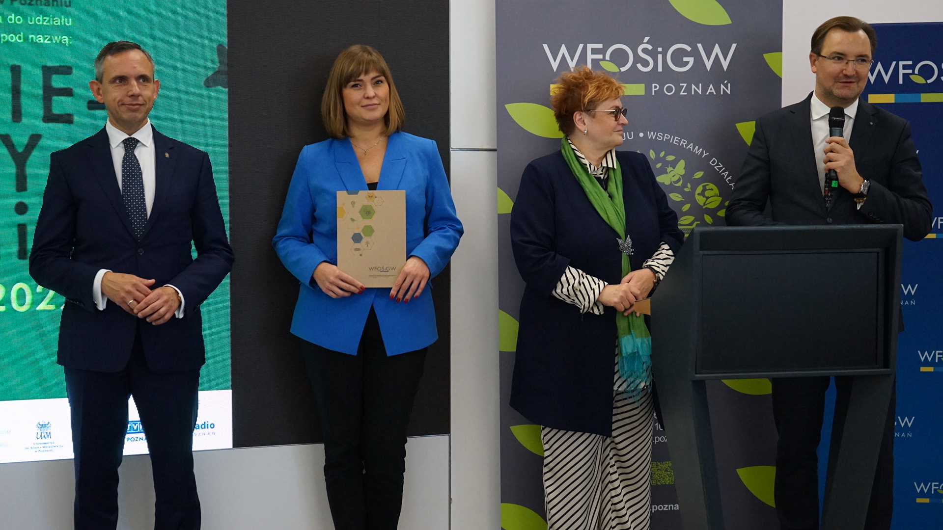 4 osoby stoją na tle ściany.