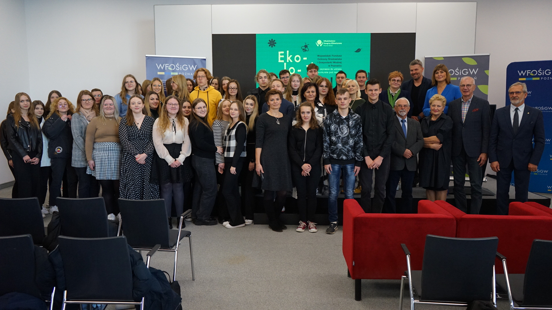 Duża grupa ludzi stoi na tle ściany.