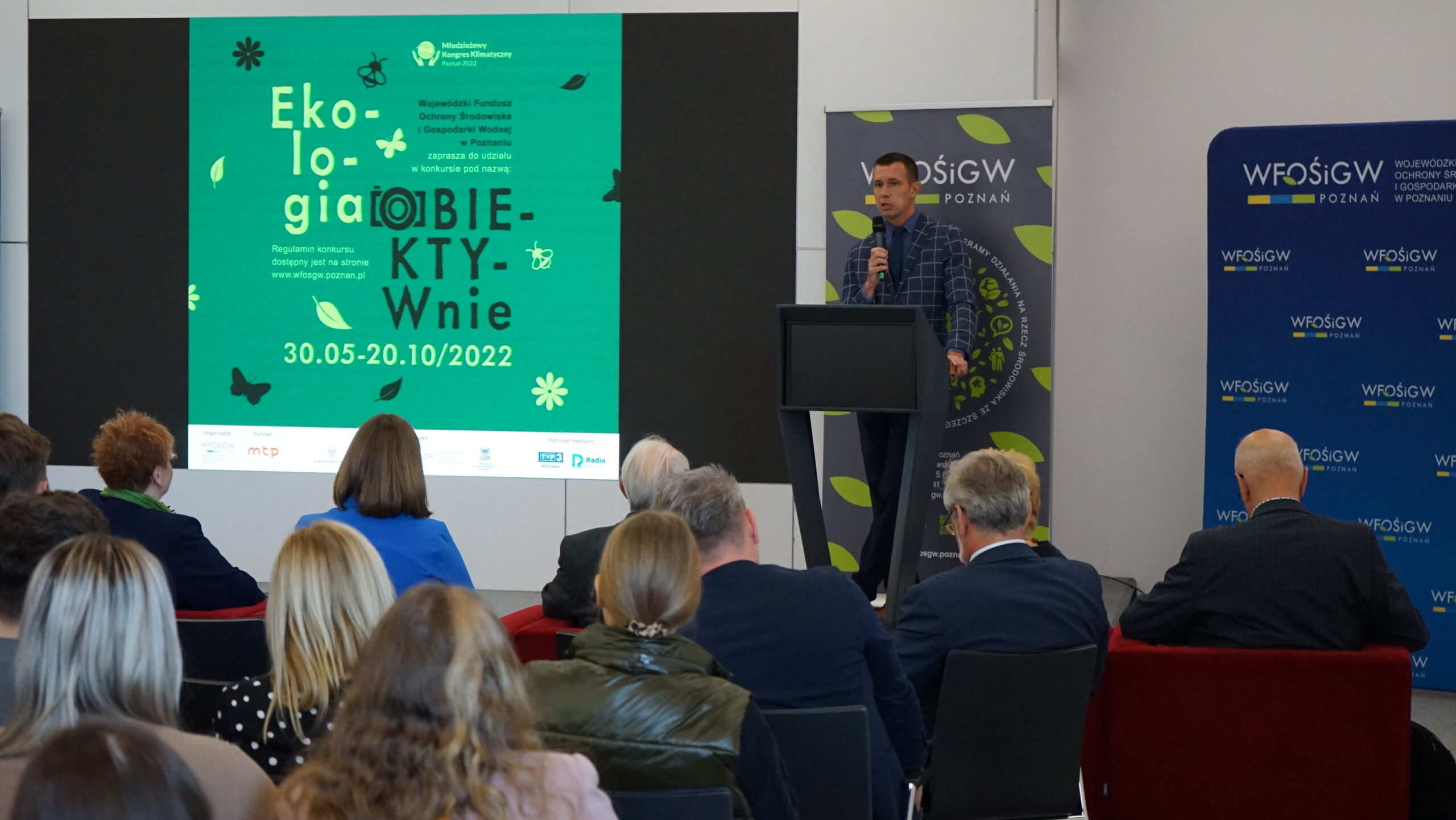 Jedna osoba stoi na scenie przy mównicy.